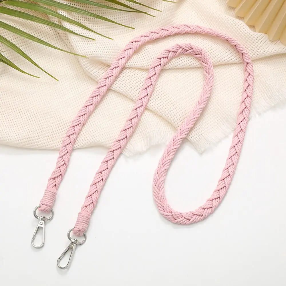 Pinkes handgewebtes Riemchen mit Metallverschlüssen auf cremefarbigem Stoffhintergrund.