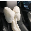 A white, fluffy bowknot car headrest pillow and lumbar support is shown placed in a black car seat.
