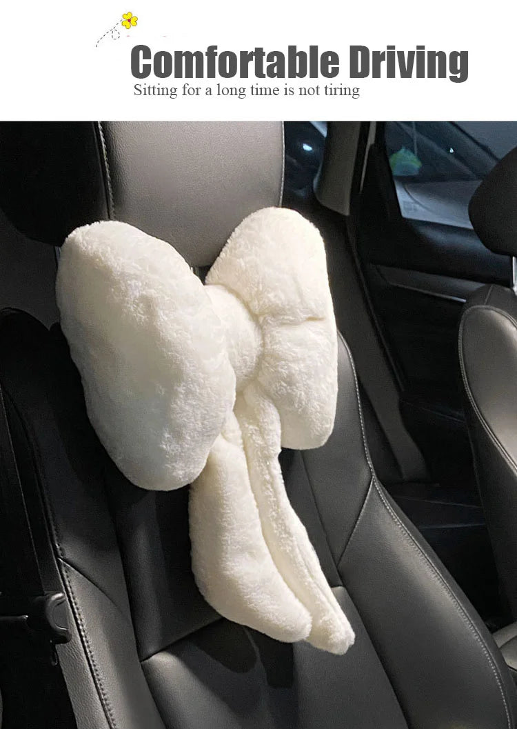 A white, fluffy bowknot car headrest pillow and lumbar support is shown placed in a black car seat.