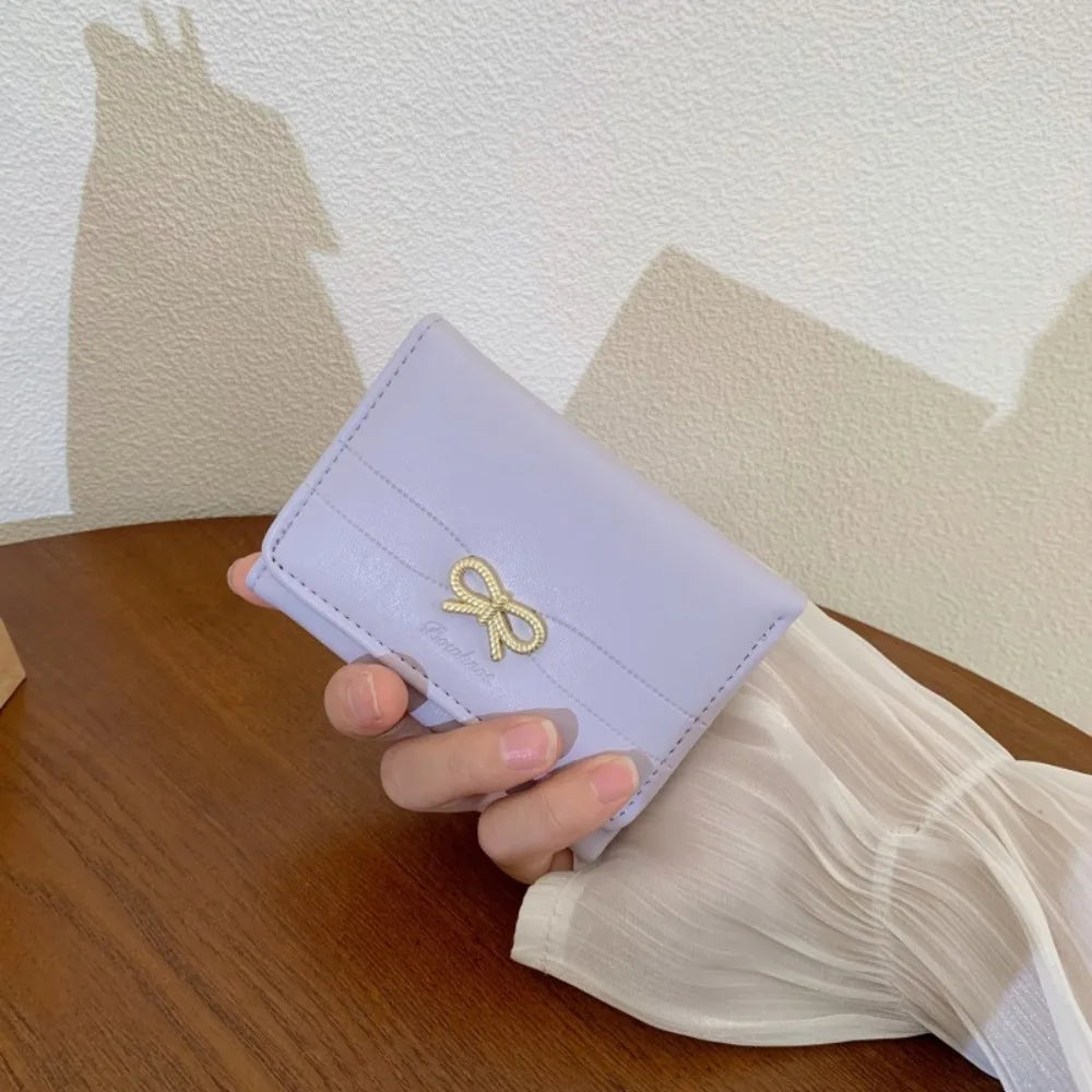 Portefeuille à trois volets violet clair en PU avec un charm de ruban or tenu dans la main d'une personne sur une surface en 