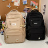 A beige lightweight nylon college backpack is displayed next to a black version in a retail setting.