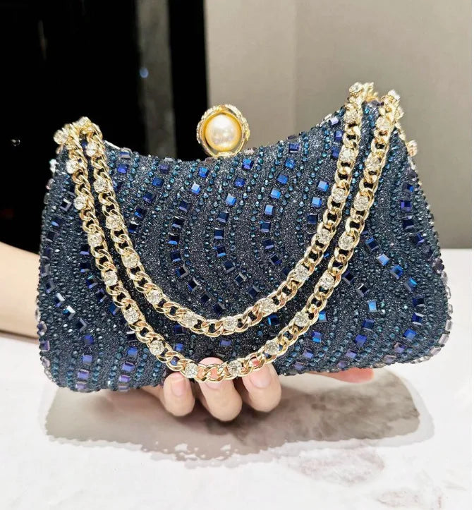 A dark blue rhinestone evening clutch adorned with gold chains and pearl accents.