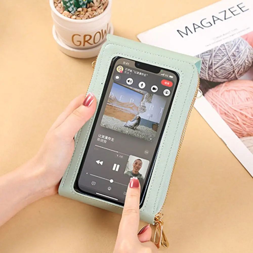 A hand holds a light green RFID-protected touch screen crossbody bag with a gold zipper, displaying a music player interface.