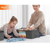 A woman is folding light blue clothing into a dark storage bag with a child watching.
