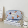A light blue and white striped cosmetic makeup bag featuring bear designs, resting on a stack of books.