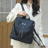 A woman is holding a black leather anti-theft backpack in front of a light beige jacket.