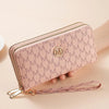 A light pink double zipper wallet with a monogram pattern and a leather strap is shown on a hand.