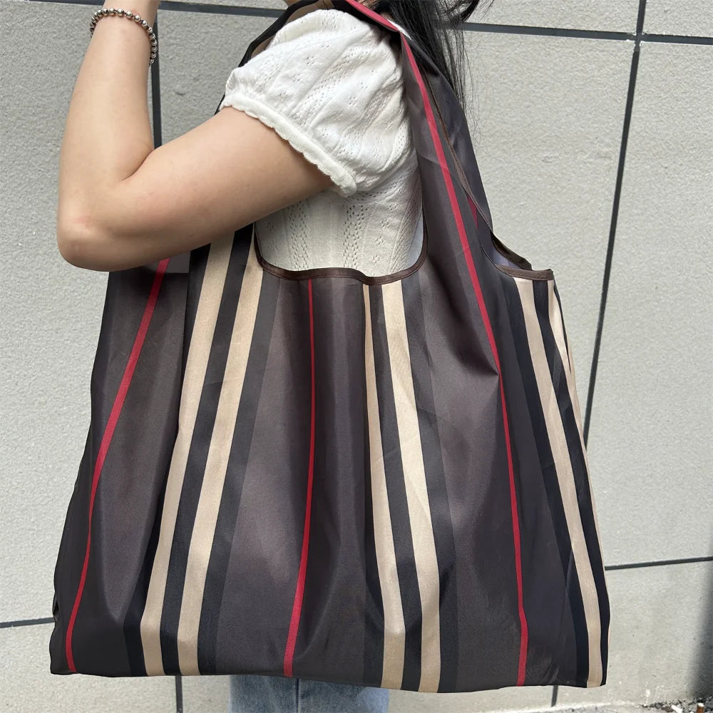 A person is holding a brown and beige striped foldable oxford grocery tote bag against a light gray background.