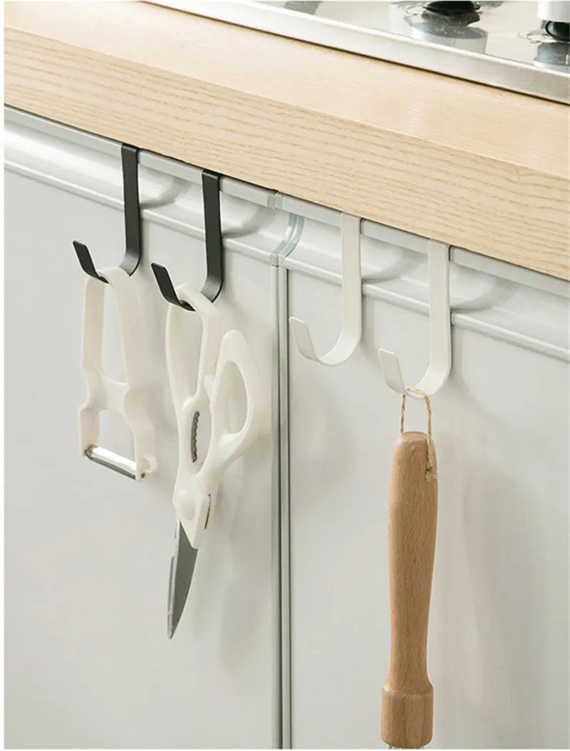 A white heavy duty multi-purpose hook rack for cabinet doors is mounted on a light wood shelf.