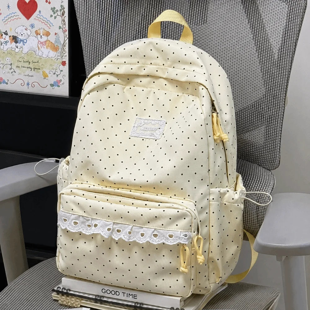 A cream-colored polka dot nylon travel backpack with light yellow straps and a white lace trim.