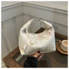 A cream embroidered crossbody shoulder bag resting on a wooden surface.
