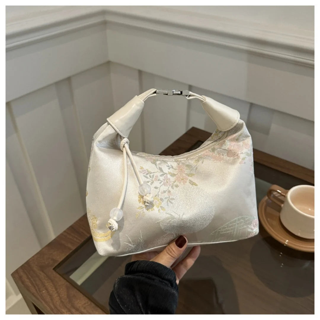 A cream embroidered crossbody shoulder bag resting on a wooden surface.