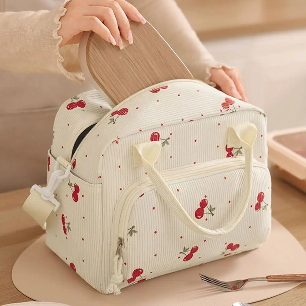 Sac de pique-nique portable en velours côtelé crème avec broderie de fruits rouges tenu par une main.