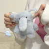 A hand holds a light blue plush elephant toy against a white background.