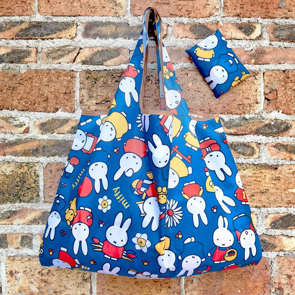 A blue Miffy folding shopping bag is displayed against a brick wall.