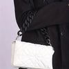 White quilted handbag with a black acrylic chunky chain shoulder strap being held by a person wearing a black coat.