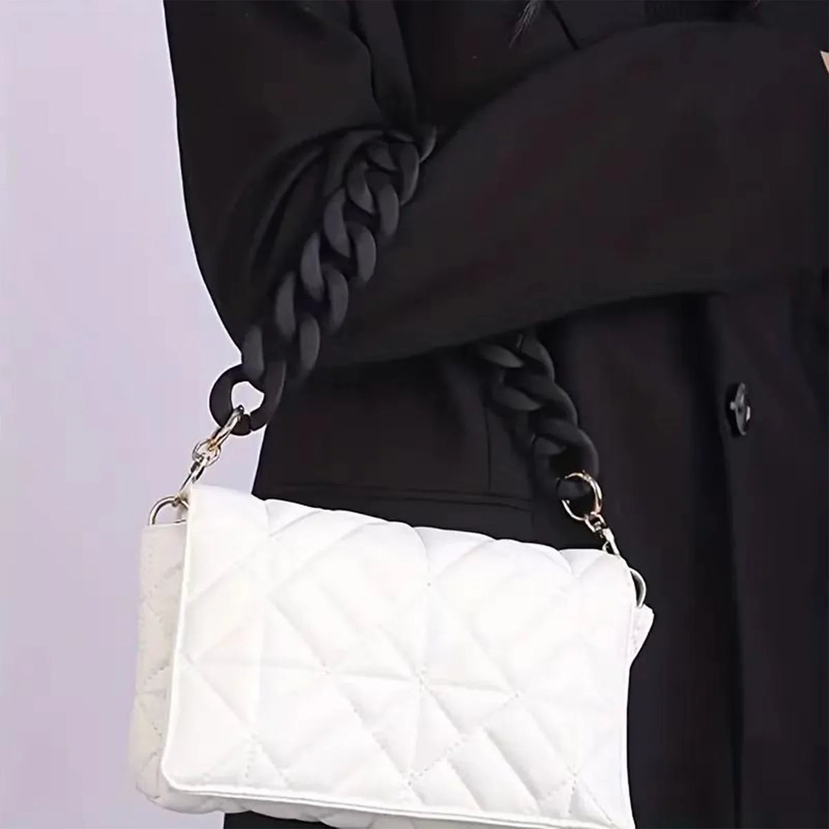 White quilted handbag with a black acrylic chunky chain shoulder strap being held by a person wearing a black coat.