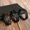 A collection of men's multi-layer leather bracelets featuring tiger eye beads displayed on a dark surface.