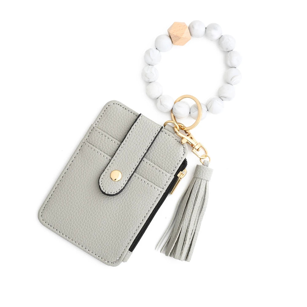 A light gray leather card holder with a flap and tassel attached to a white bead bracelet.