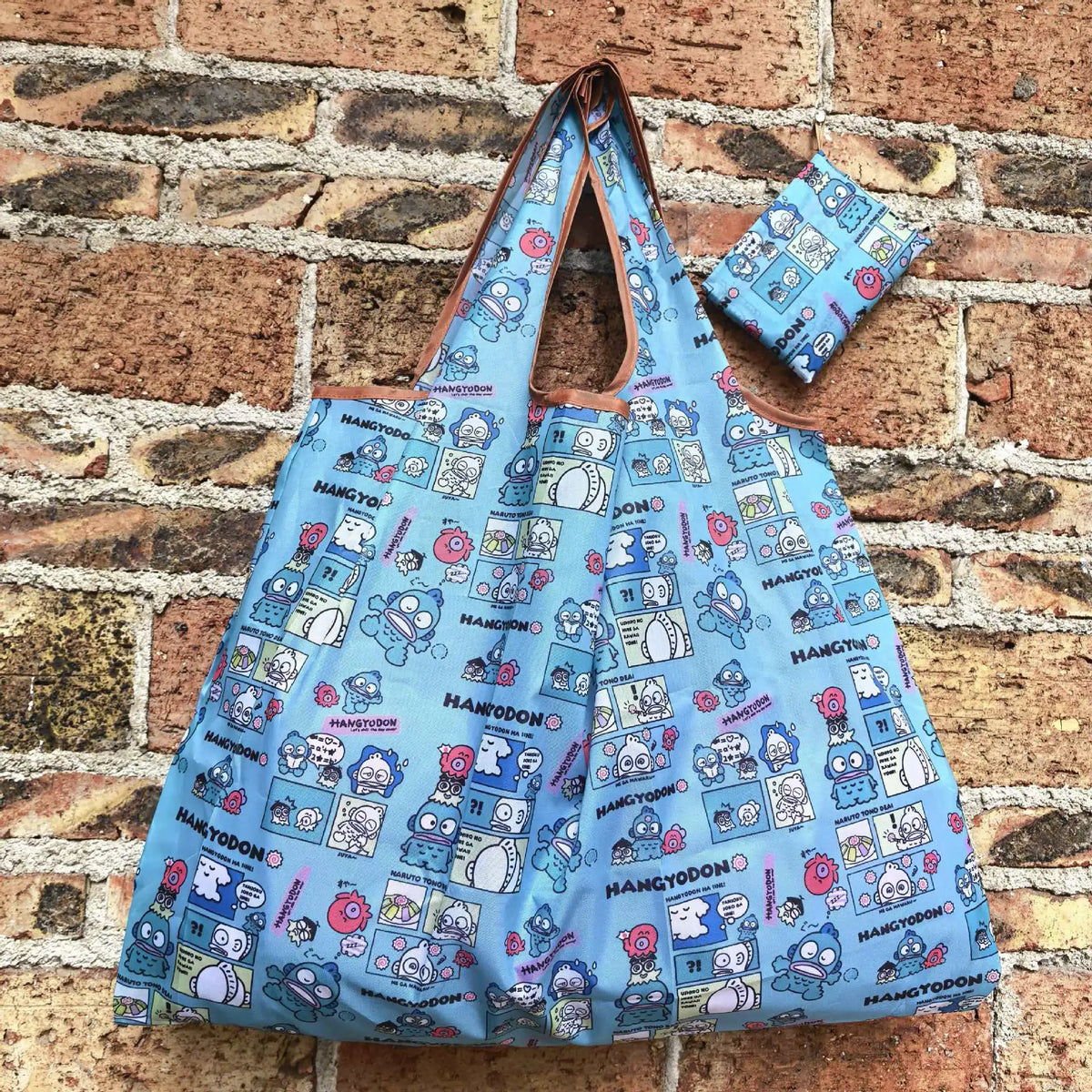 A light blue reusable shopping bag featuring a pattern of cartoon characters and text on a brick background.