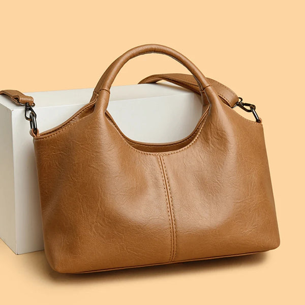 A tan leather women's casual crossbody shoulder bag with a zip closure resting on a white box.