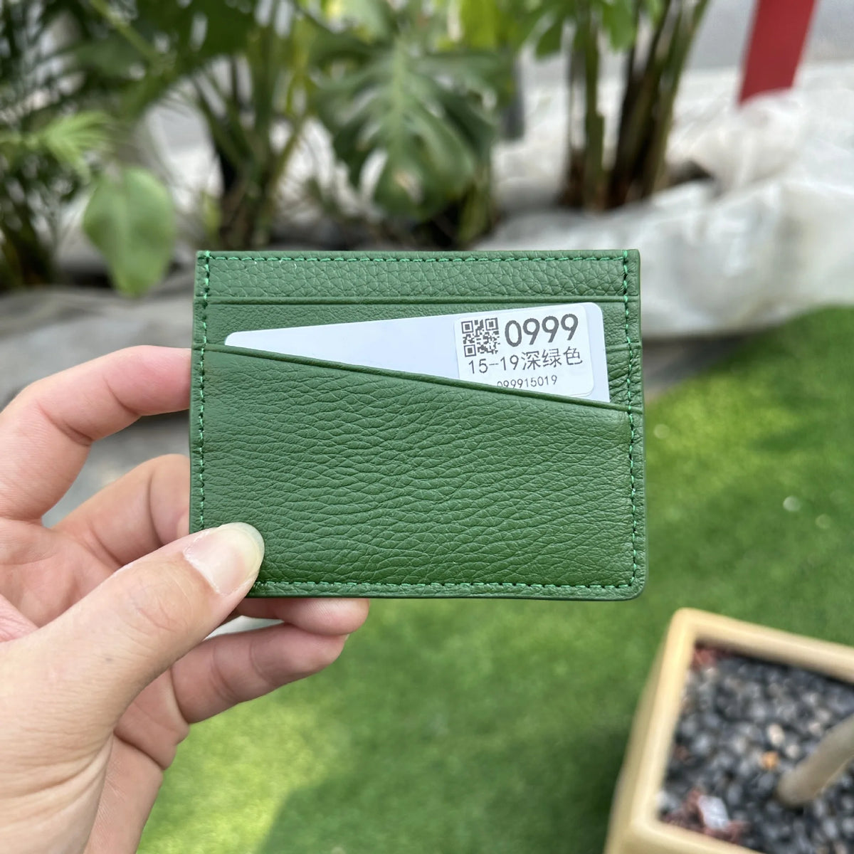 Une main tient un porte-cartes en cuir vert avec une étiquette blanche affichant le numéro 0999.