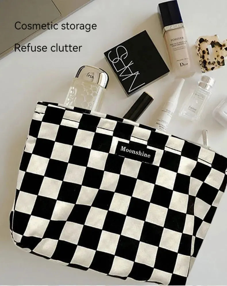A black and white checkered cosmetic storage bag next to various beauty products like perfume and skincare.