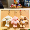 Three plush rabbit fur keychains in white, pink, and tan displayed on a wooden board.