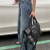A person holding a black saddle-shaped PU leather city tote bag next to a white car.