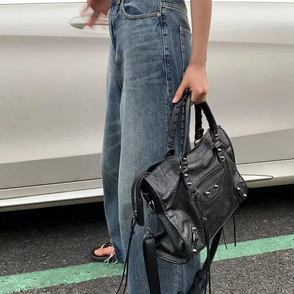 A person holding a black saddle-shaped PU leather city tote bag next to a white car.