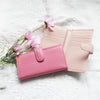 A pink leather card holder and coin purse resting on a white textured fabric with pink flowers.