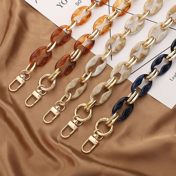 Colección de cadenas para bolsos de acrílico en tonos ámbar, beige y azul sobre tela marrón.