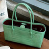 A light green croc embossed leather tote bag with a handle and magnetic closure resting on a wooden surface.