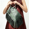 A woman holds a green leather fringed clutch bag with tassels against a dark red dress.