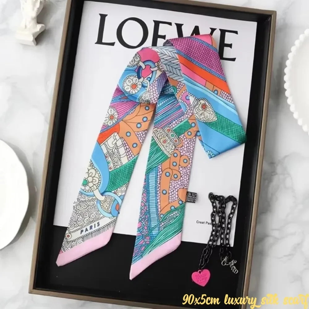 A colorful silky twill ribbon scarf featuring various patterns and colors displayed in a framed picture.