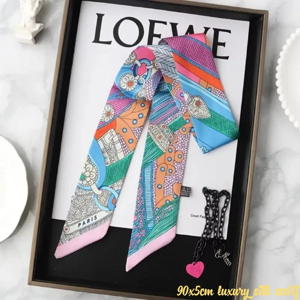 A colorful silky twill ribbon scarf featuring various patterns and colors displayed in a framed picture.