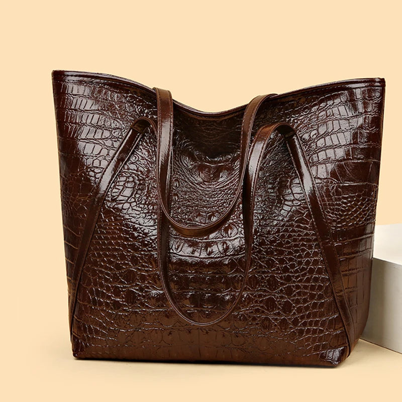 A dark brown crocodile print tote bag with leather handles shown in a studio setting.