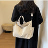 A beige corduroy multi-pocket tote bag is held by a person wearing a black dress.