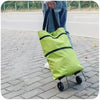A person is holding a bright lime green foldable lightweight shopping cart with black straps and wheels on a paved surface.