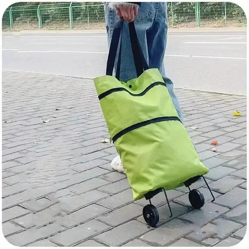 A person is holding a bright lime green foldable lightweight shopping cart with black straps and wheels on a paved surface.