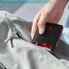 A hand is inserting a black card wallet into a gray jacket pocket, highlighting the slim and modern design.