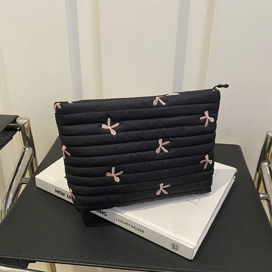 Black embroidered makeup pouch with a zipper resting on a white box.