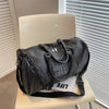 A black crocodile grain PU leather travel duffle bag resting on a light-colored chair next to a window.