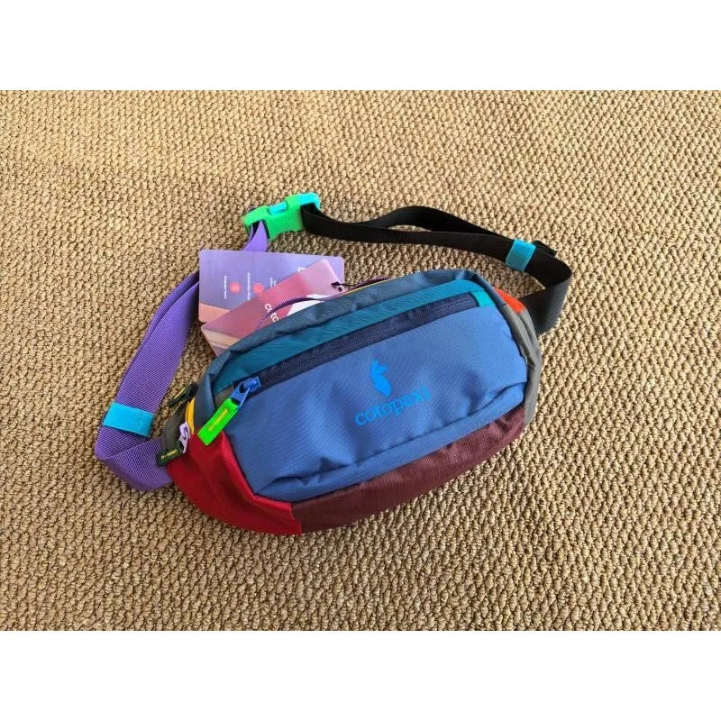 A patchwork color block fanny pack featuring purple, pink, blue, and red fabric against a beige background.