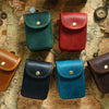 A collection of five leather waist bags in various colors including green, red, brown, black, and blue, arranged on an old ma