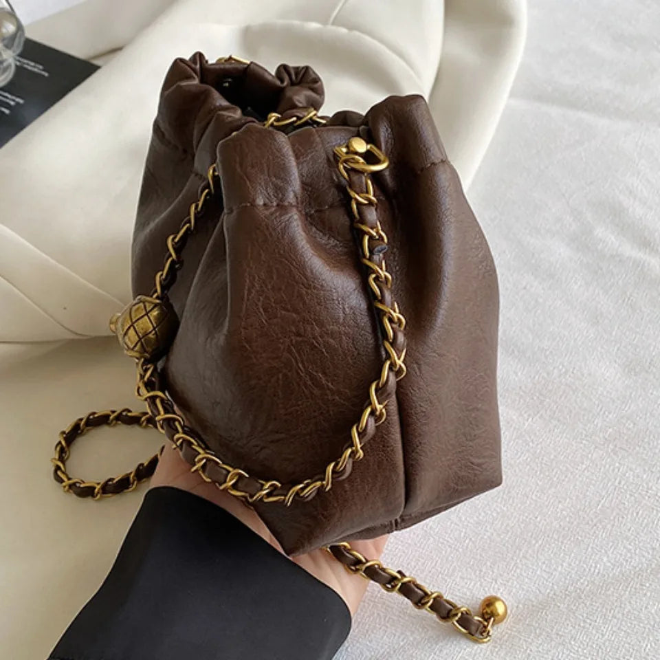 A dark brown PU leather chain shoulder bag resting on a white surface.