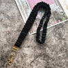 Schwarzes gerafftes Lanyard mit goldenem Schlüsselclip auf einer strukturierten grauen Oberfläche.