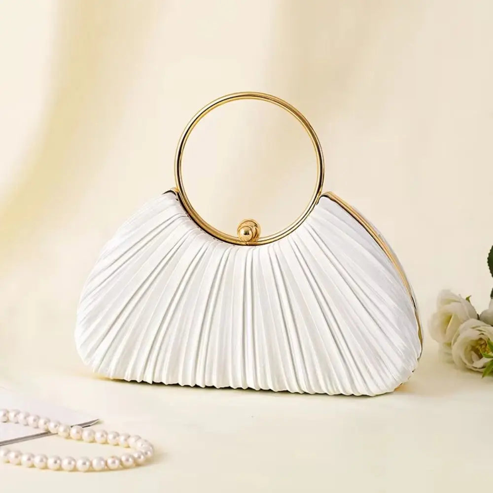 A white satin pleated evening clutch bag with a gold circular handle resting on a light surface.