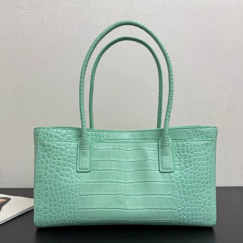 A mint green crocodile print leather handbag with a top handle is displayed on a dark surface.