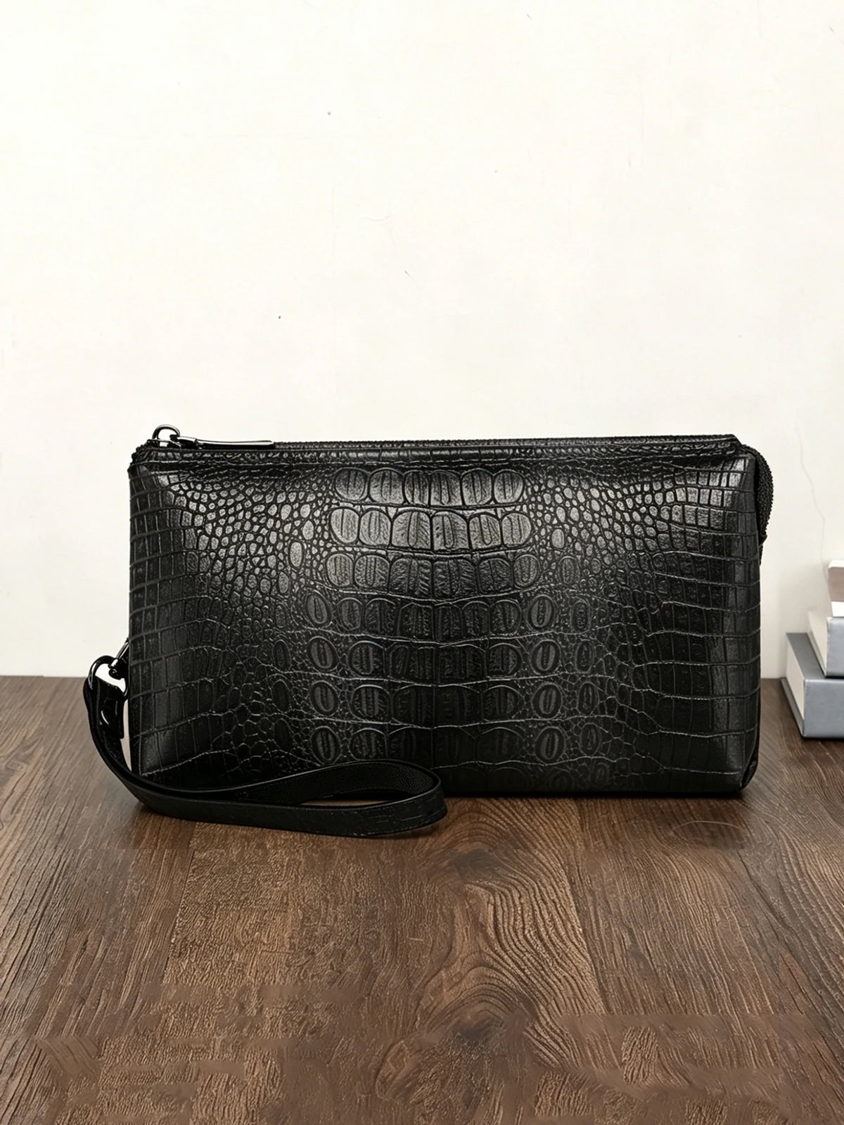 Clutch de estampado de cocodrilo negro sobre una superficie de madera oscura.